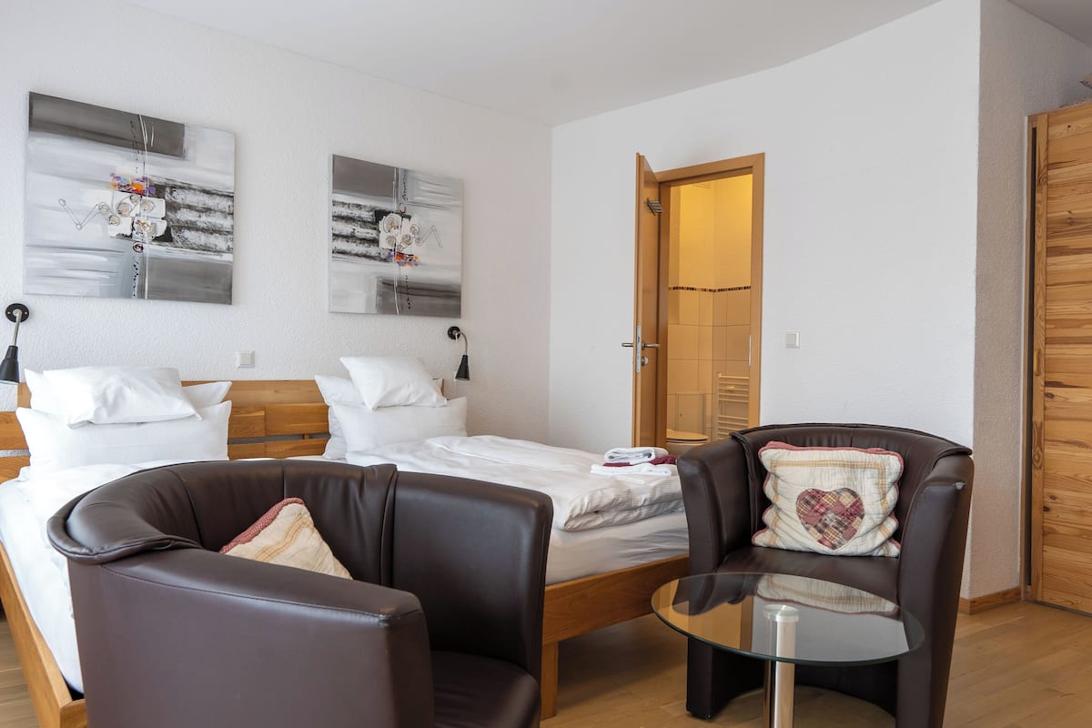 A hotel room with two beds, a sitting area with a chair and a small table, and artwork on the walls.