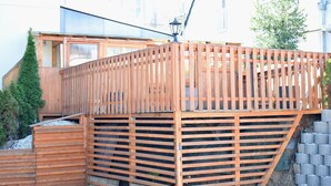 Eine Holzterrasse mit geneigtem Dach, einer Treppe, die zu einem Gebäude führt, und einem Laternenpfahl.