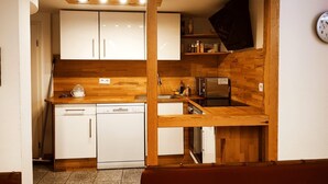 Eine kleine Küche mit weißen Schränken, einer Holz Arbeitsplatte, einem Geschirrspüler und einer Mikrowelle.