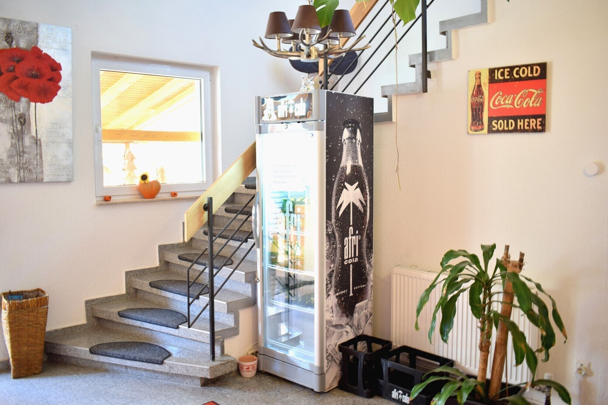 A staircase with a glass enclosure leading to a landing, a Coca-Cola sign, and a potted plant.