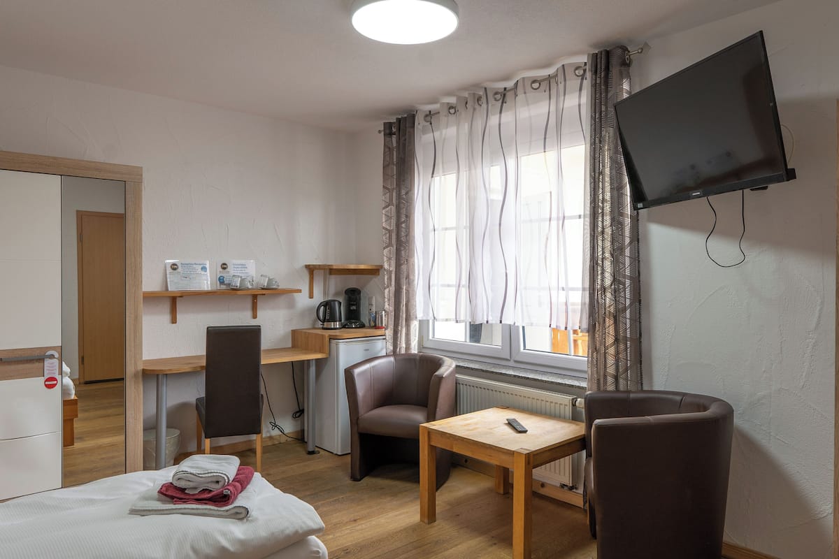 A hotel room with a bed, a desk, a chair, a TV mounted on the wall, and a window with curtains.
