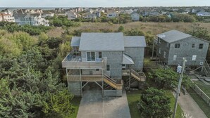 A two-story house with a wooden deck, a staircase, and a small attached garage. - Prime Location, Short Walk To The Beach, Water Views, Sun Deck (Rodanthe)