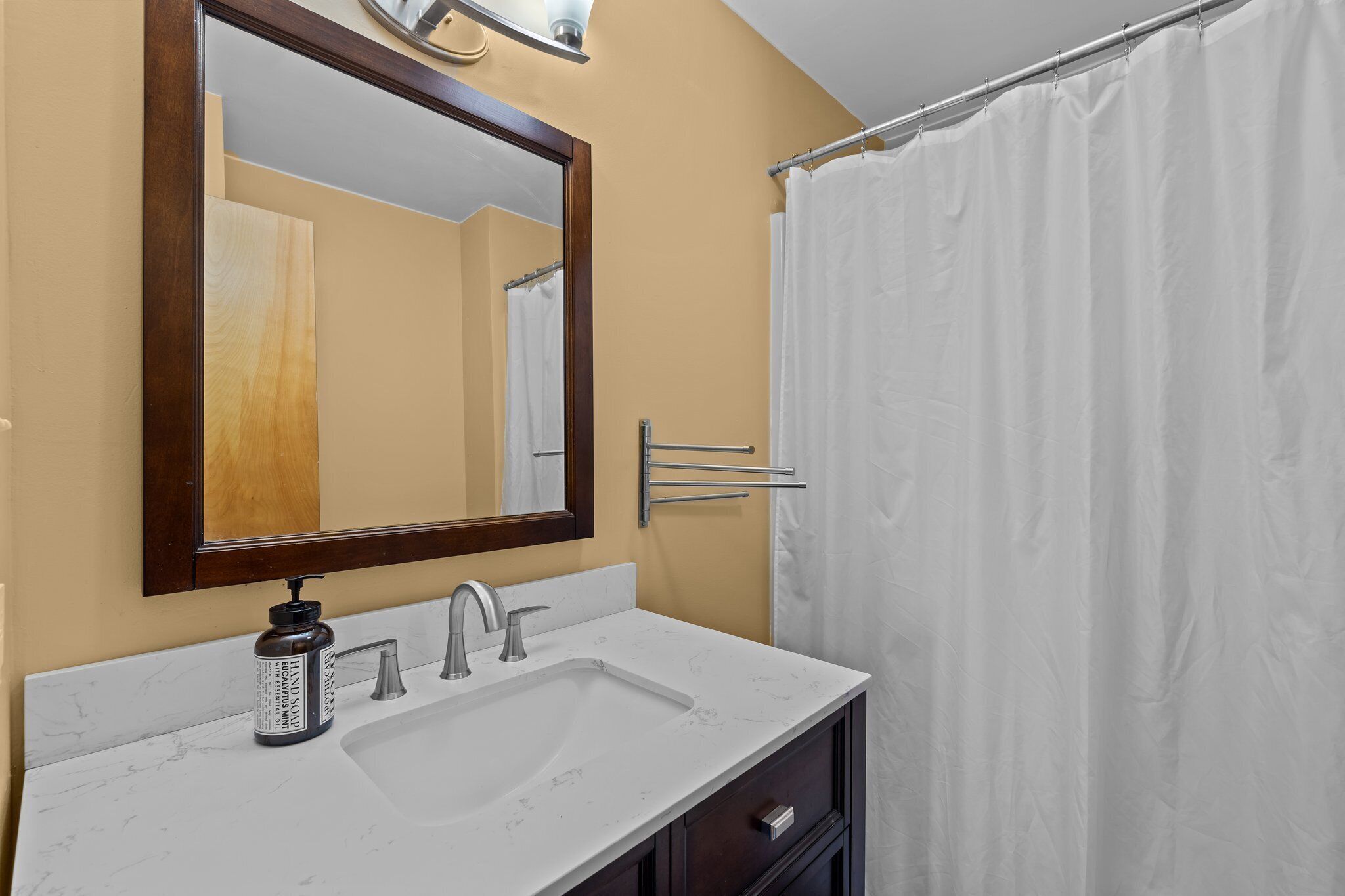 Une salle de bain avec un lavabo blanc, un miroir, un porte-serviettes et un rideau de douche.