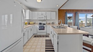 A modern kitchen with white cabinets, a built-in oven, a microwave, and a large island with a sink. - Prime Location, Short Walk To The Beach, Water Views, Sun Deck (Rodanthe)