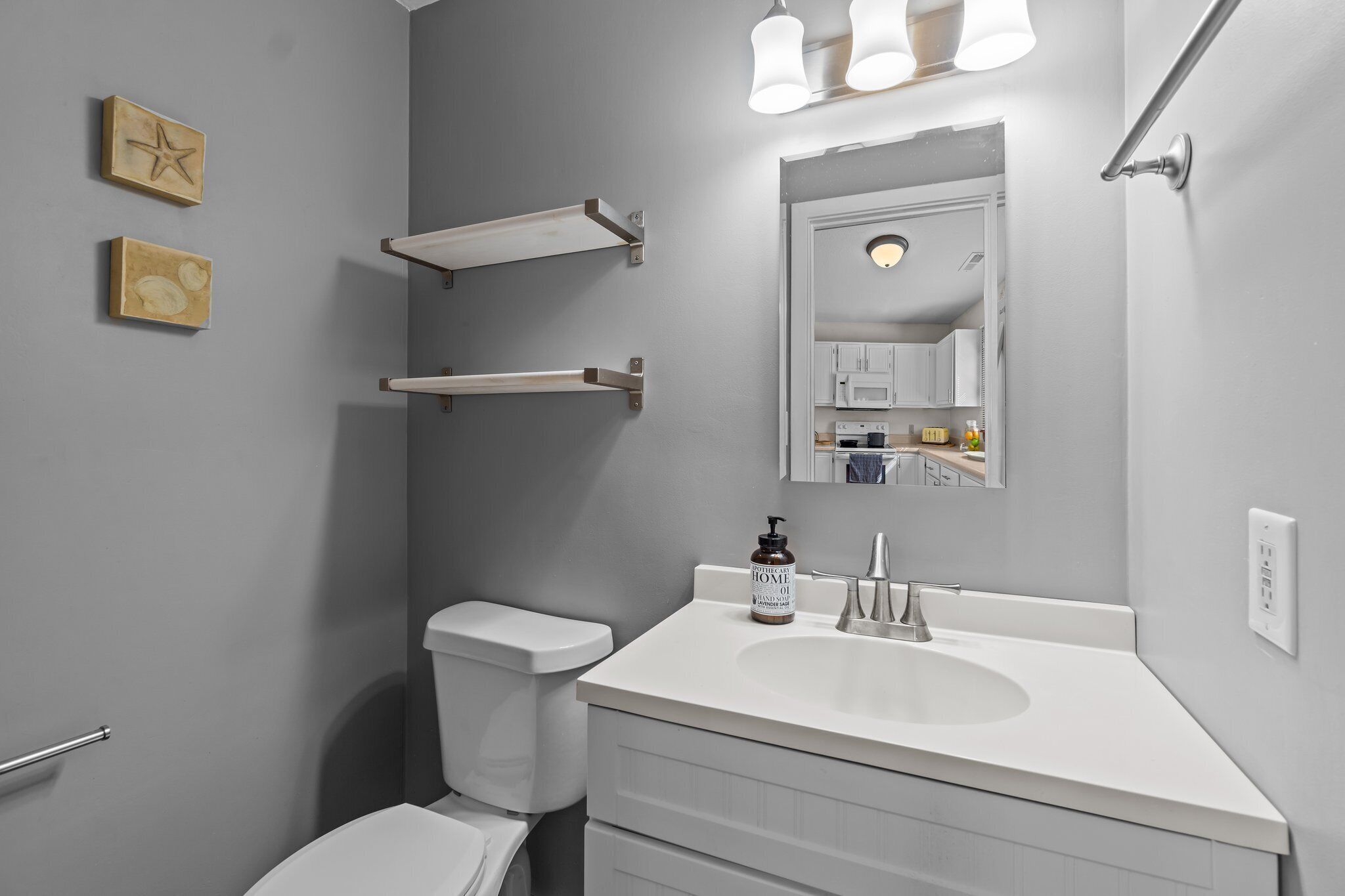 A modern bathroom with a white sink, a mirror, and a toilet. There are two wall-mounted shelves and a star-shaped decoration.