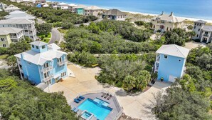 Una zona residencial costera con varias casas de dos pisos, una piscina y una playa al fondo.
