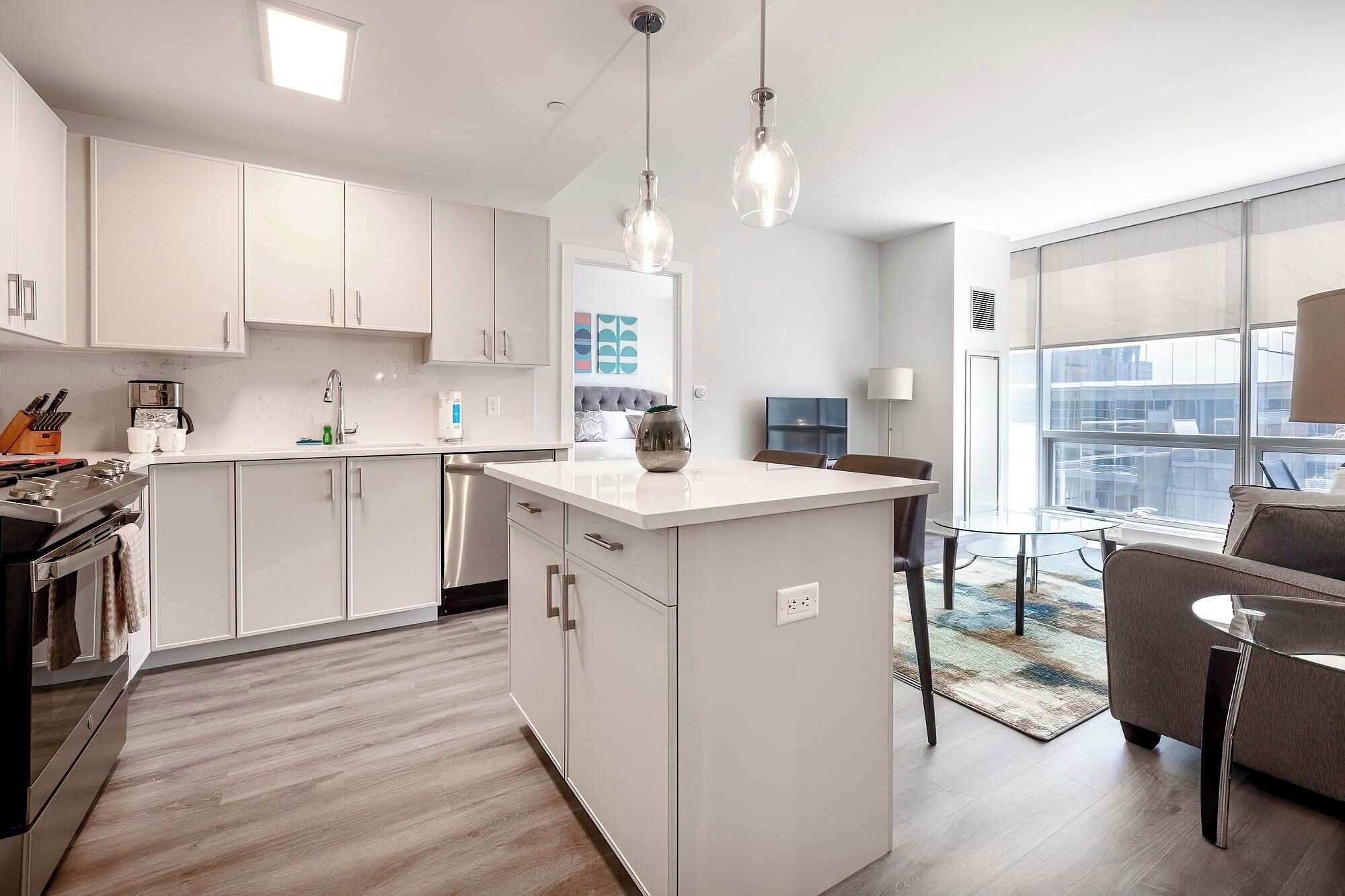 A modern kitchen with white cabinetry, a central island, and a dining area with a glass table and chairs.
