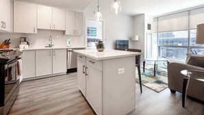 A modern kitchen with white cabinetry, a central island, and a dining area with a glass table and chairs. - Luxury Apt Near Downtown (Stamford)