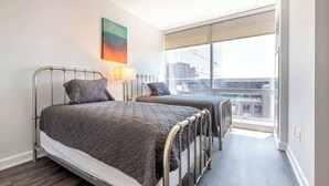 A modern bedroom with two beds, a large window, and a city view. - Luxury Apt Near Downtown (Stamford)