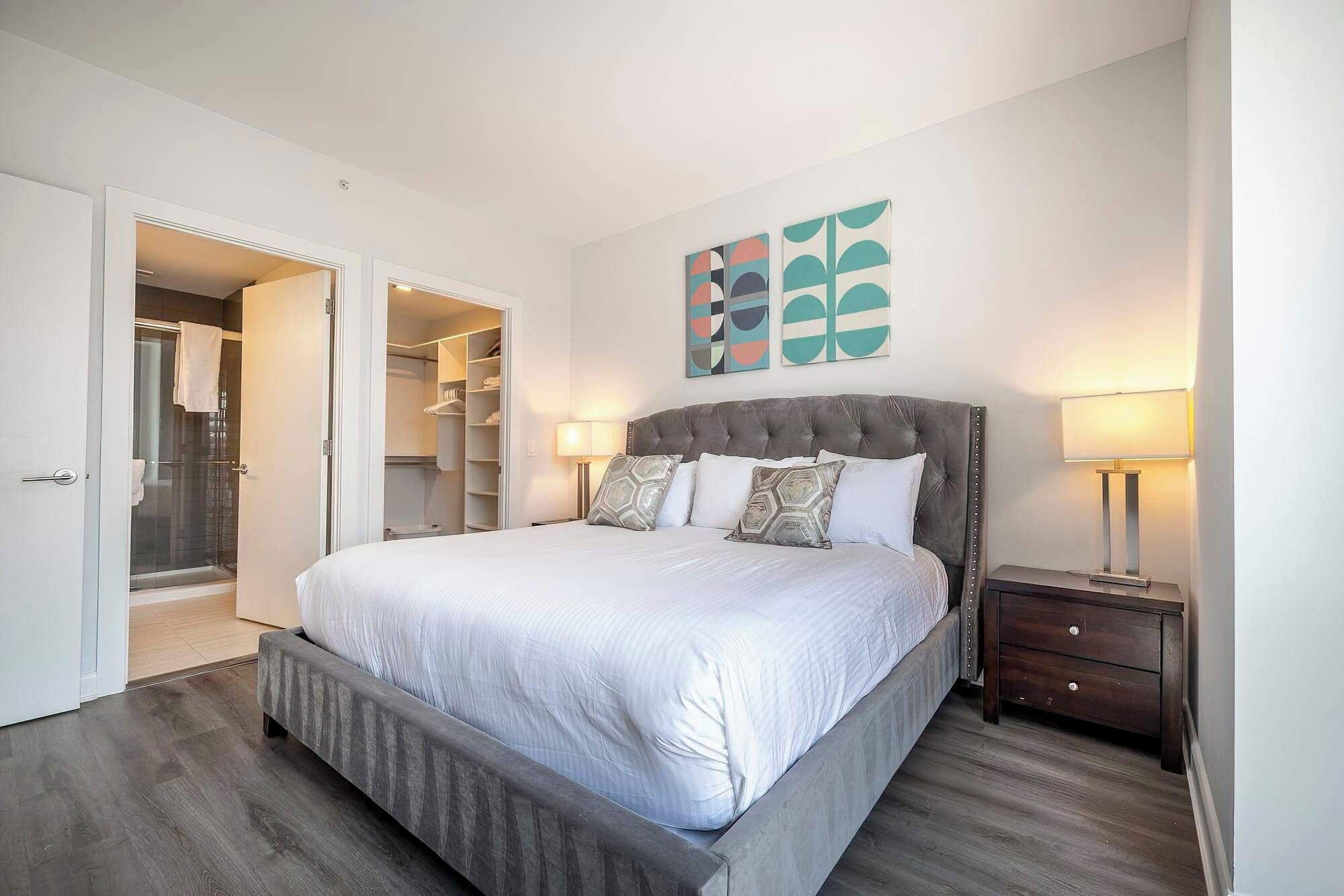 A bedroom with a large bed, a walk-in closet, and a bathroom with a glass shower.