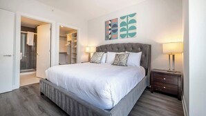 A bedroom with a large bed, a walk-in closet, and a bathroom with a glass shower. - Luxury Apt Near Downtown (Stamford)