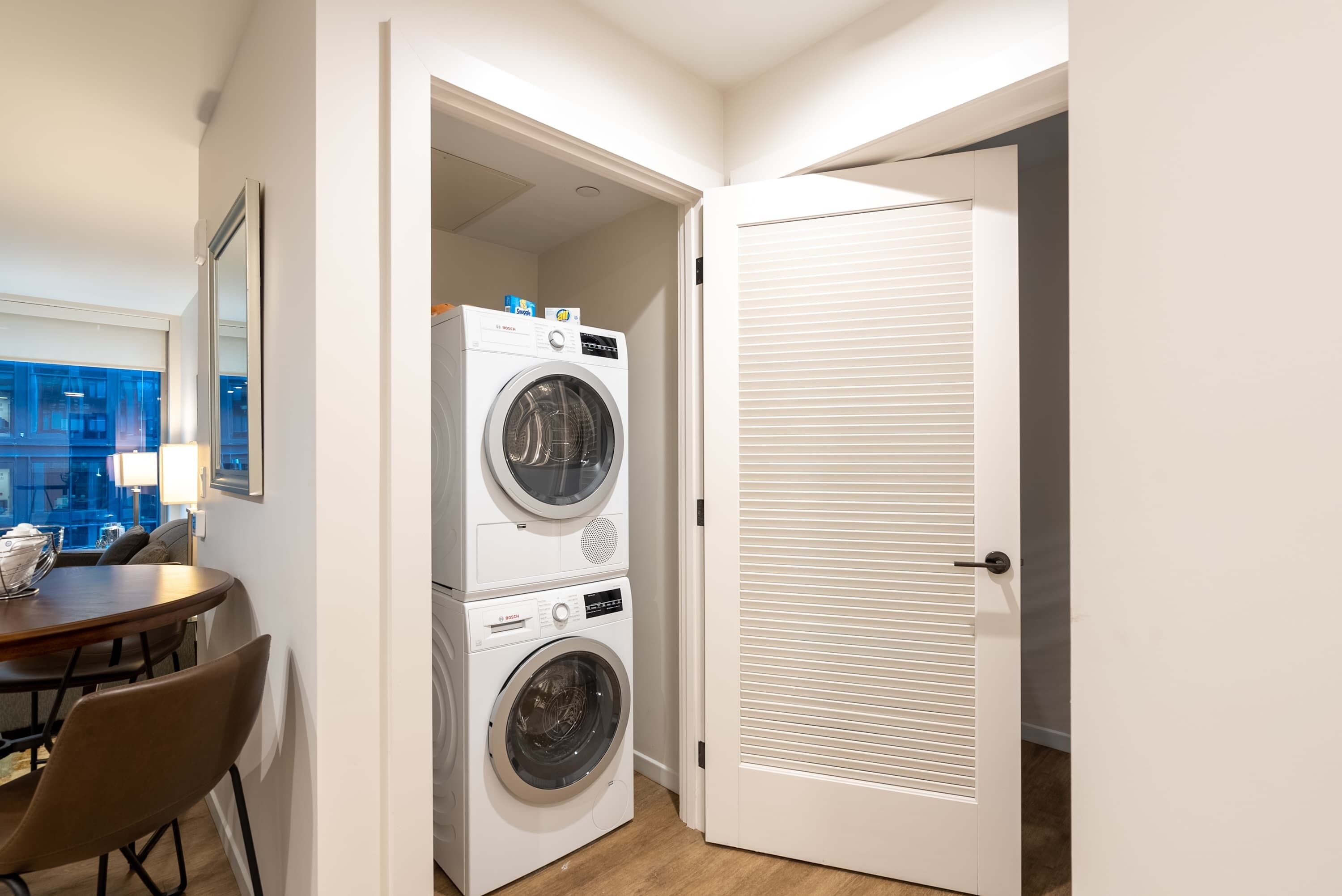 Un espace buanderie avec des lave-linge et des sèche-linge superposés, une table à manger avec des chaises et une porte à panneaux ajourés.