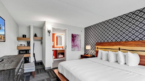 A hotel room with a bed, a desk, a chair, a small kitchenette, and a bathroom.