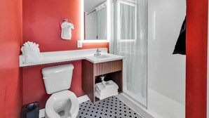 Une salle de bain moderne avec un mur d’accent rouge, des toilettes blanches, un lavabo avec un miroir au-dessus et une cabine de douche en verre.