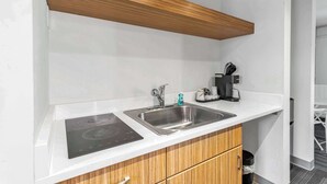 Una kitchenette con un lavamanos de acero inoxidable, una cafetera y una cocina de inducción integrada.