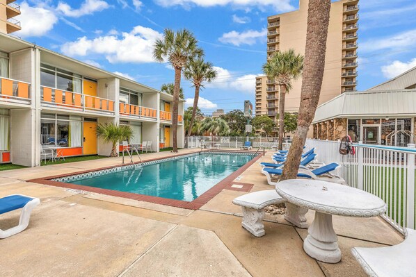 Un hotel con piscina, mobiliario exterior y palmeras.