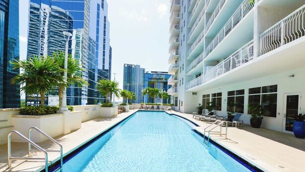 A swimming pool with a clear blue water surface, surrounded by high-rise buildings and palm trees. - 1BR Brickell | Free Parking | Metromover Access (Miami)