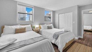 A hotel room with two beds, a window with a city view, a door, and a small bedside table with a lamp. - 1BR Brickell | Free Parking | Metromover Access (Miami)