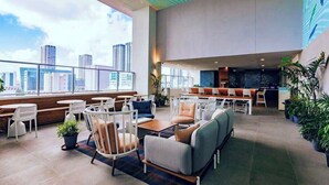 Et moderne loungeområde med siddepladser, en bar og udsigt til byens skyline.