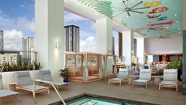 Et moderne poolområde indendørs med liggestole, en lille pool og et loft med abstrakte designs.