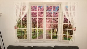 A window with a view of trees and a path, a dark-colored sofa with cushions, and a white wall.