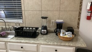 A kitchen with a sink, a blender, a coffee maker, and a trash can.
