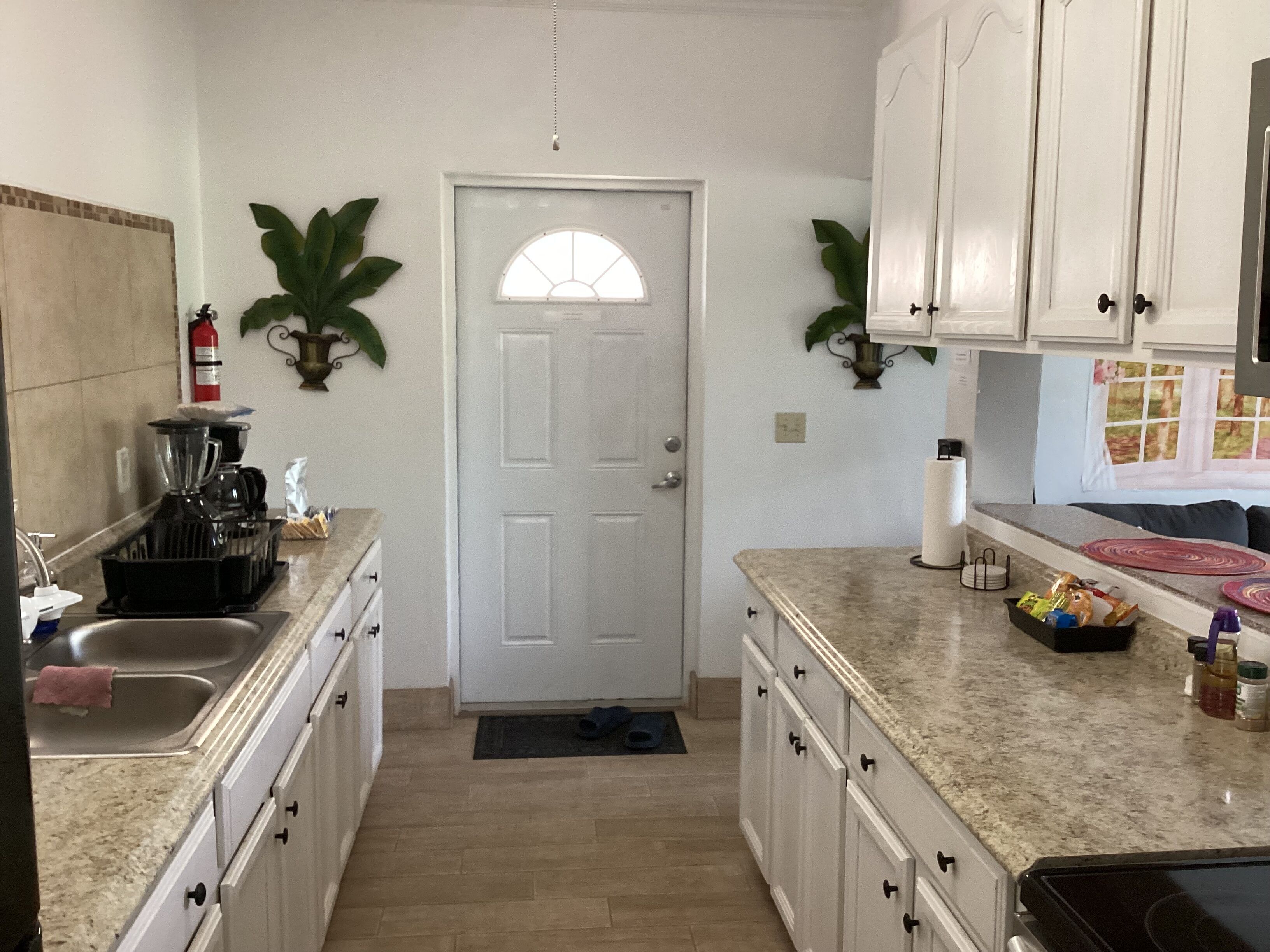 A kitchen with white cabinets, a coffee maker, a sink, and a door with a window.