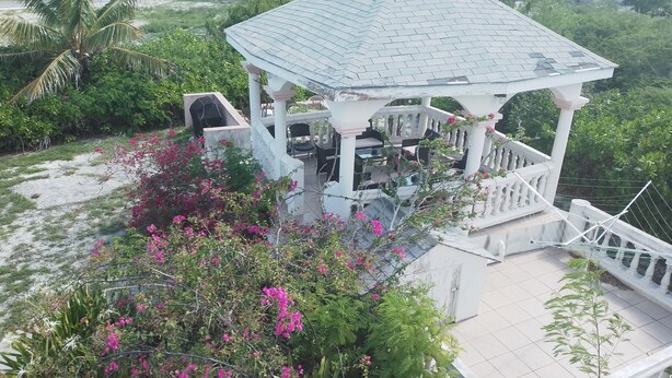 A gazebo with a tiled roof, surrounded by lush greenery and pink flowers.