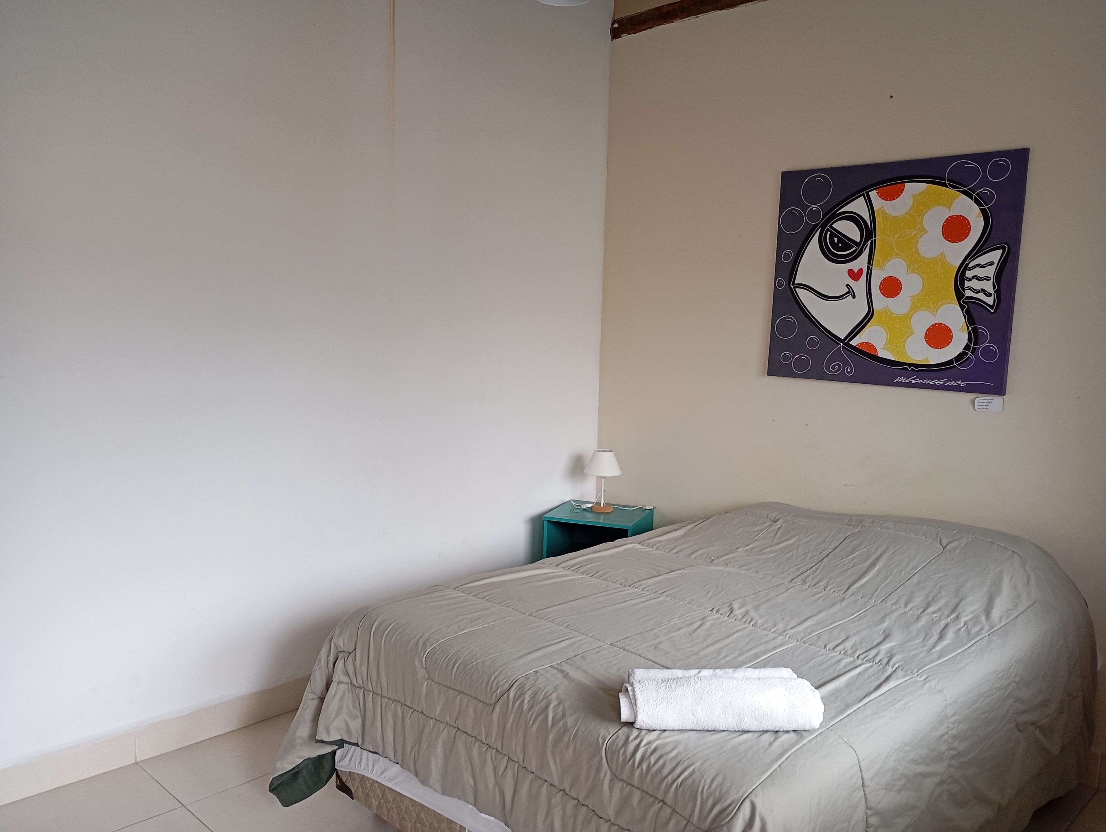 Un dormitorio con cama, mesita de noche, lámpara y un cuadro en la pared.