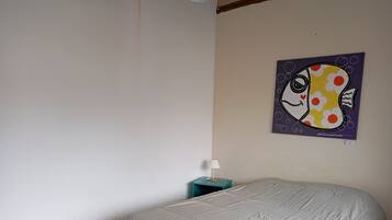 Un dormitorio con cama, mesita de noche, lámpara y un cuadro en la pared.
