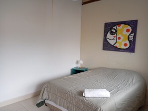 Un dormitorio con cama, mesita de noche, lámpara y un cuadro en la pared.