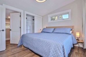 Un dormitorio con cama, mesita de noche, ventana y armario abierto.