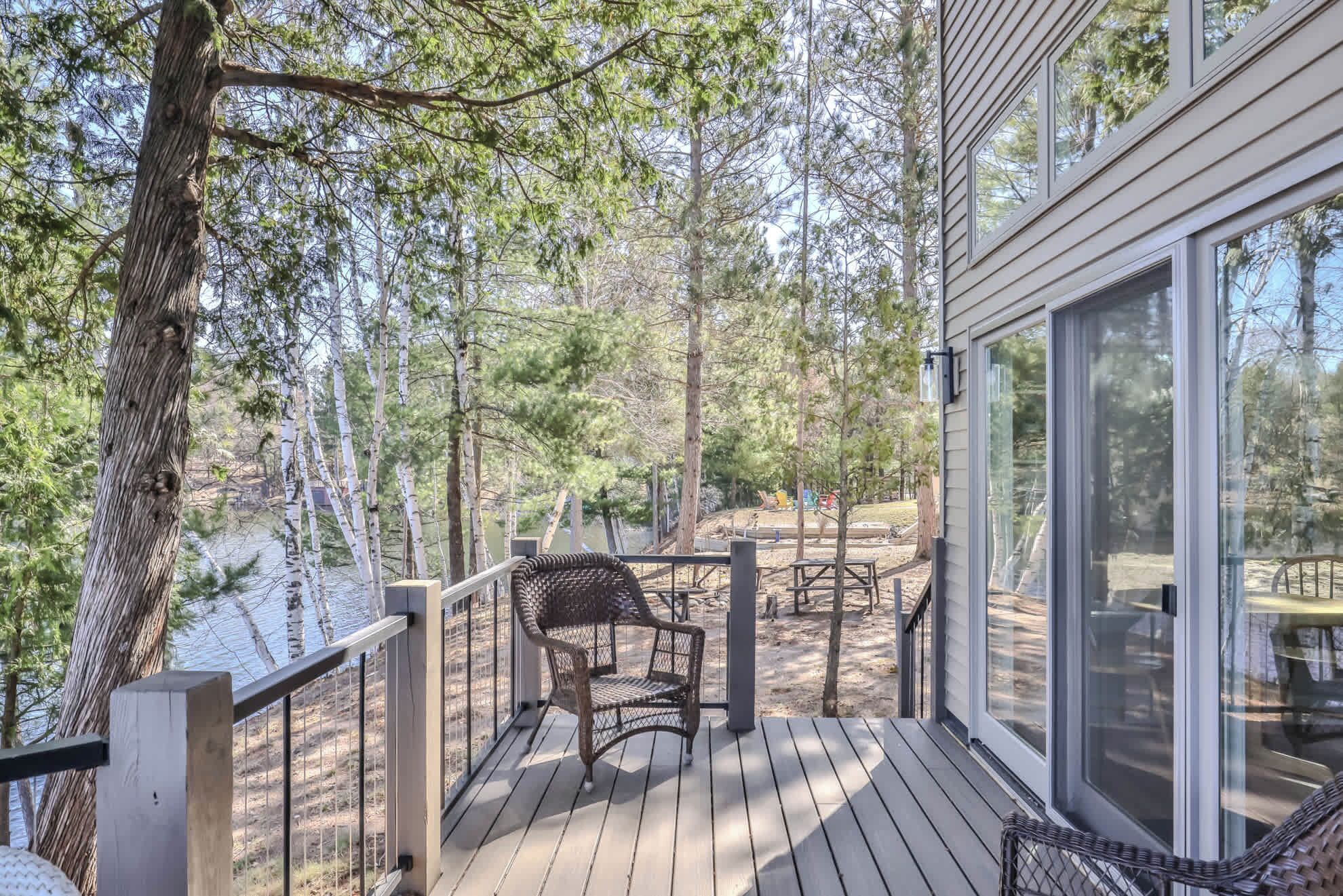 A wooden deck with a metal railing, a wicker chair, and a table.