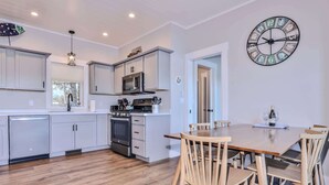 Una cucina moderna con mobili bianchi, forno integrato e microonde. C'è un'area pranzo con tavolo e sedie in legno.
