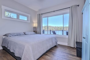 Un dormitorio con una cama grande, una ventana con cortinas, una mesita de noche y vistas a un balcón.