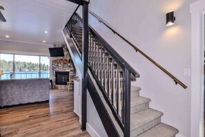 A modern interior with a wooden staircase, a stone fireplace, and a view of a lake through large windows.