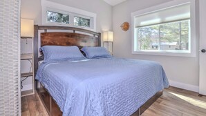 Een slaapkamer met een bed, nachtkastje, lamp, raam en uitzicht op de omgeving.