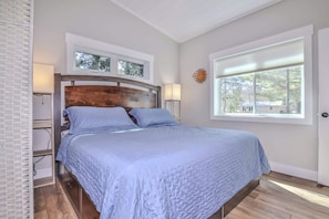 A bedroom with a bed, a nightstand, a lamp, a window, and a view of the outdoors. - Eikedahls' Shoreview Cottage (Minocqua)