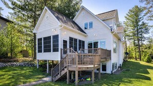 A two-story house with a deck, a covered outdoor area, and a stone wall. - Eikedahls' Shoreview Lake House (Minocqua)