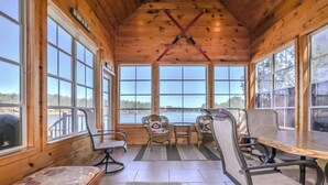 A wooden cabin with large windows, a wooden ceiling, and a view of a lake. There are four chairs and a bench. - Eikedahls' Shoreview Lake House (Minocqua)