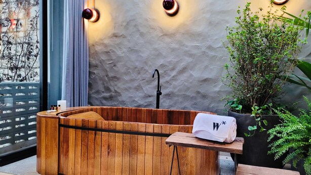 A wooden bathtub with a towel and a bottle, a potted plant, and a textured wall with pendant lights. - 6BR Designer Retreat With Jacuzzi Near Provenza (Medellín)