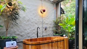 A wooden bathtub with a black faucet, surrounded by potted plants and a small stool with a white cloth. - 6BR Designer Retreat With Jacuzzi Near Provenza (Medellín)