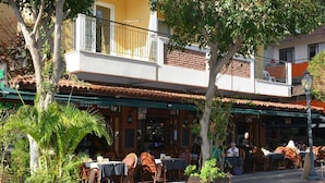An outdoor cafe with tables and chairs, a building with a balcony, and a sign for a pizza restaurant. - Kleopatra Hotel (Alanya)