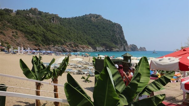 A beach with umbrellas, lounge chairs, and a view of a mountain. - Kleopatra Hotel (Alanya)