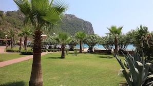 A well-maintained garden with palm trees and a clear view of a mountainous landscape in the background. - Kleopatra Hotel (Alanya)