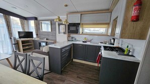 Une cuisine compacte équipée d’un four à micro-ondes, d’une cuisinière et d’un évier, un coin repas avec une table et des chaises, et un téléviseur placé dans un coin.