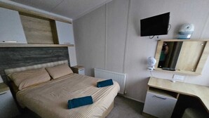 Une chambre à coucher comprenant un lit, une table de chevet, un bureau, une chaise et un téléviseur fixé au mur.