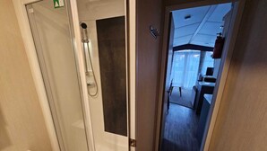 Une chambre d’hôtel dotée d’une douche en verre, d’une petite table de chevet et donnant sur la chambre voisine.