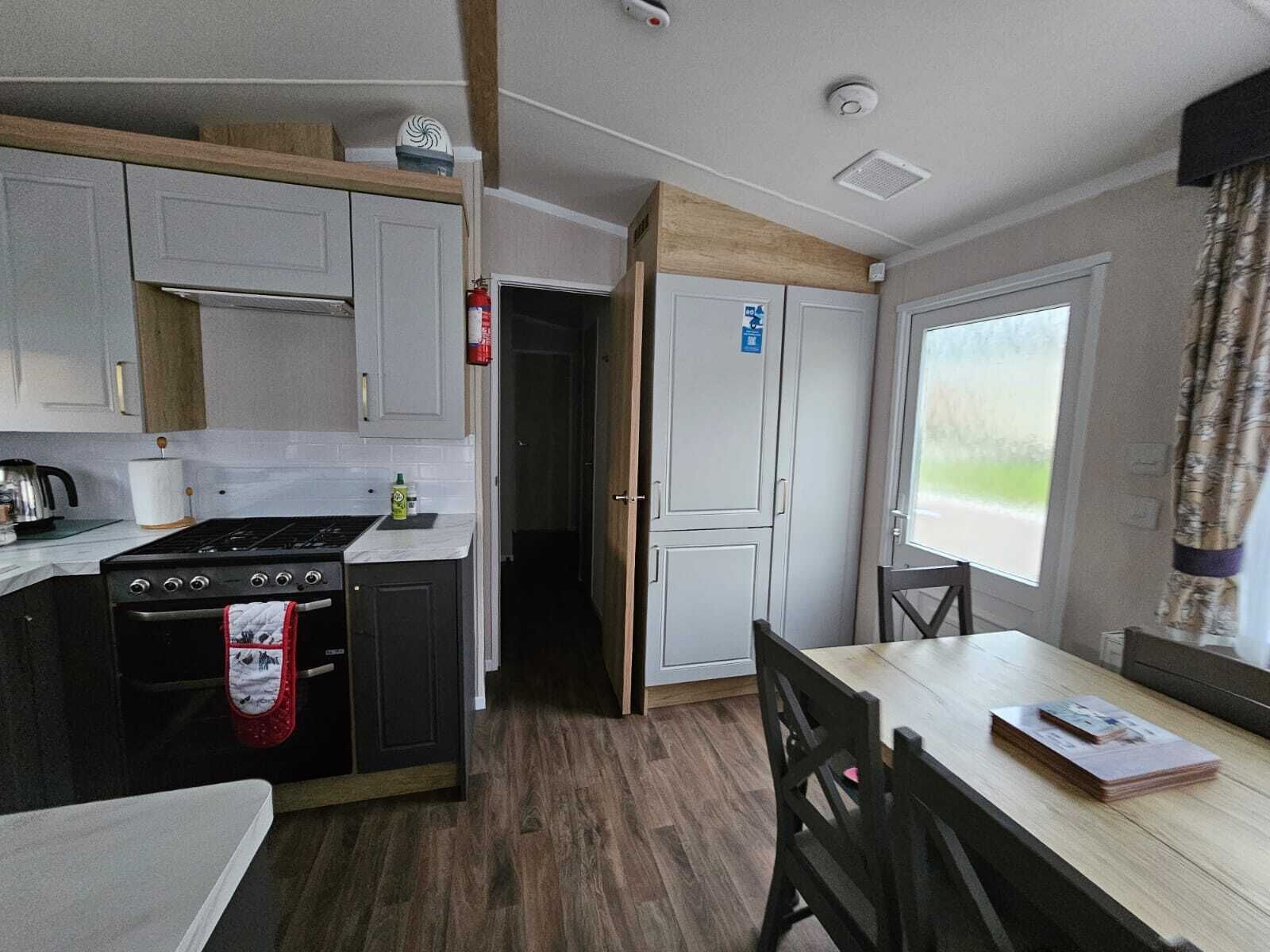 Eine kleine Küche mit Herd, Backofen und Schränken. Ein Esstisch mit Stühlen und ein Fenster mit Aussicht.