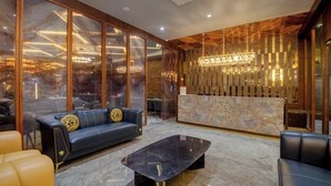 A modern lobby with a marble reception desk, leather seating, and a chandelier. - Hotel Diamond 26 (Surat)